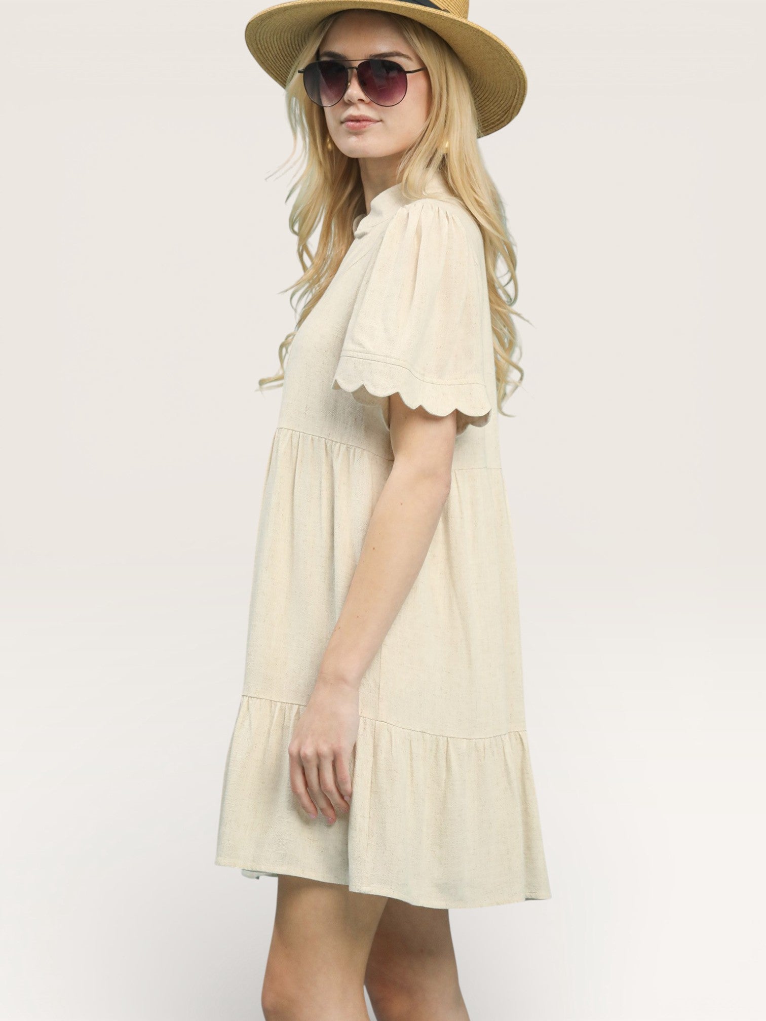 Woman wearing a cream dress with ruffled sleeves and a hat on a white background