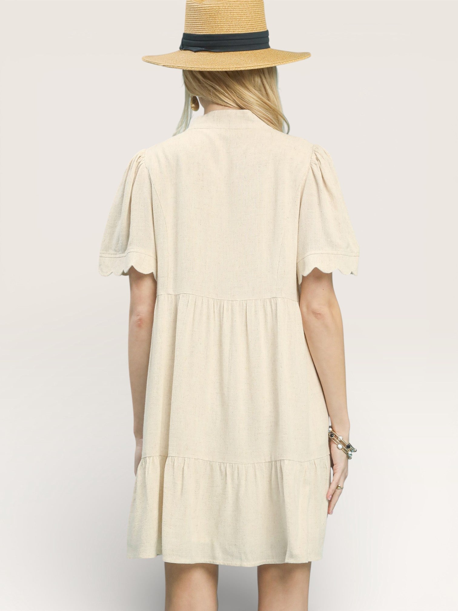 Woman wearing a beige dress and straw hat on a plain background