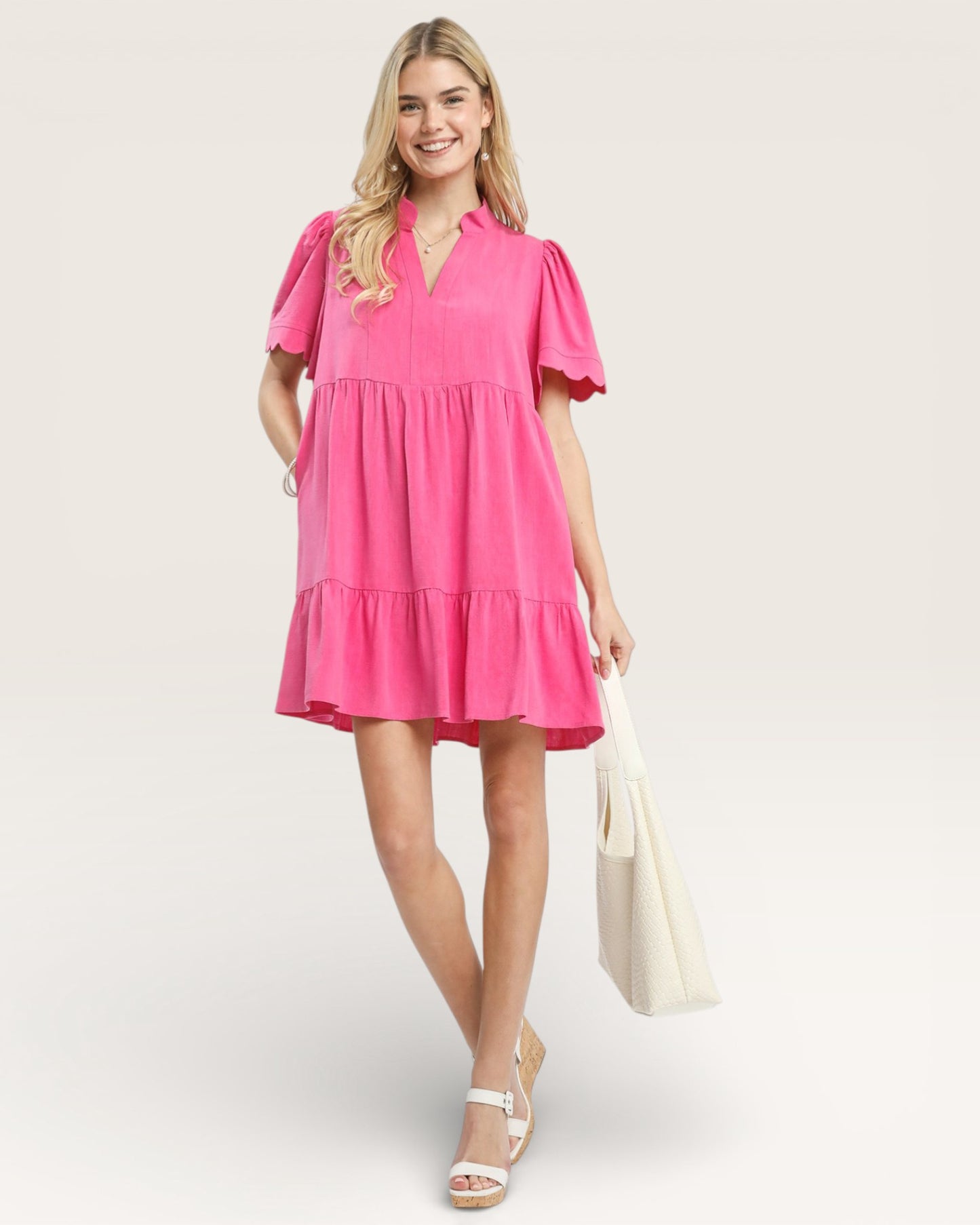 Woman wearing a pink dress holding a white bag on a light background