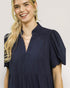 Woman wearing a navy blue dress with puffed sleeves on a plain background