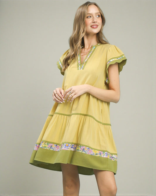 Woman wearing a yellow dress with floral embroidery on a plain background