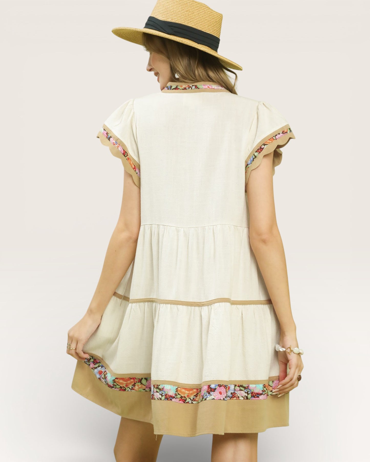 Woman wearing a cream-colored dress with floral embroidery and a straw hat on a plain background