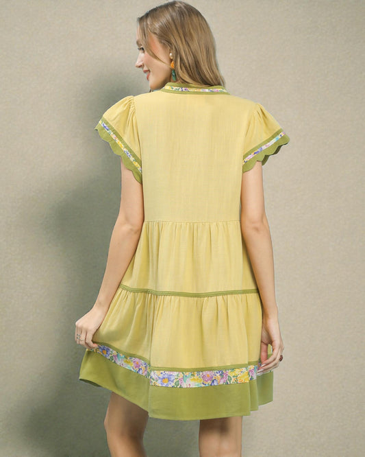 Woman wearing a yellow dress with floral trim against a beige background