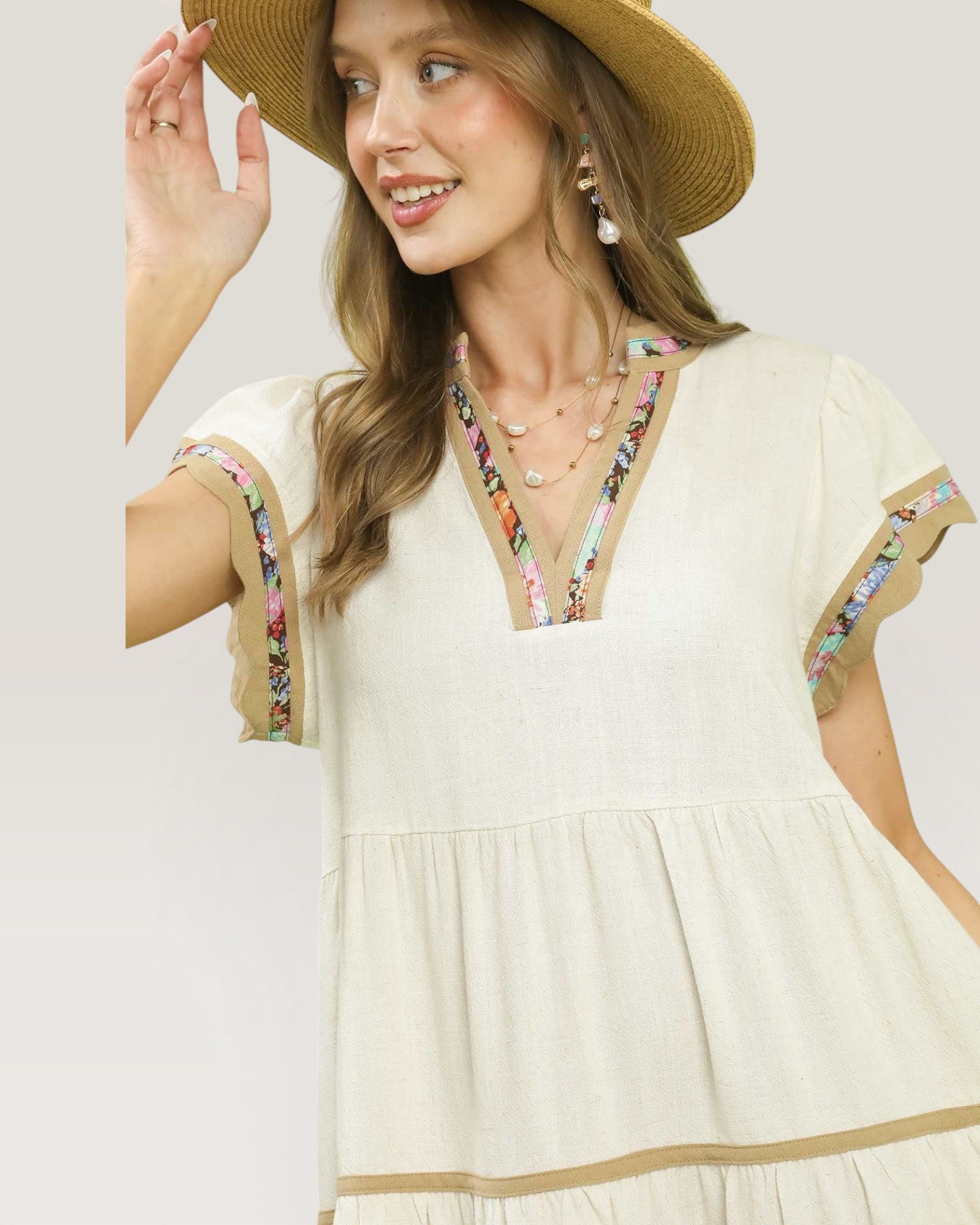Woman wearing a white dress with floral embroidery and a straw hat on a plain background