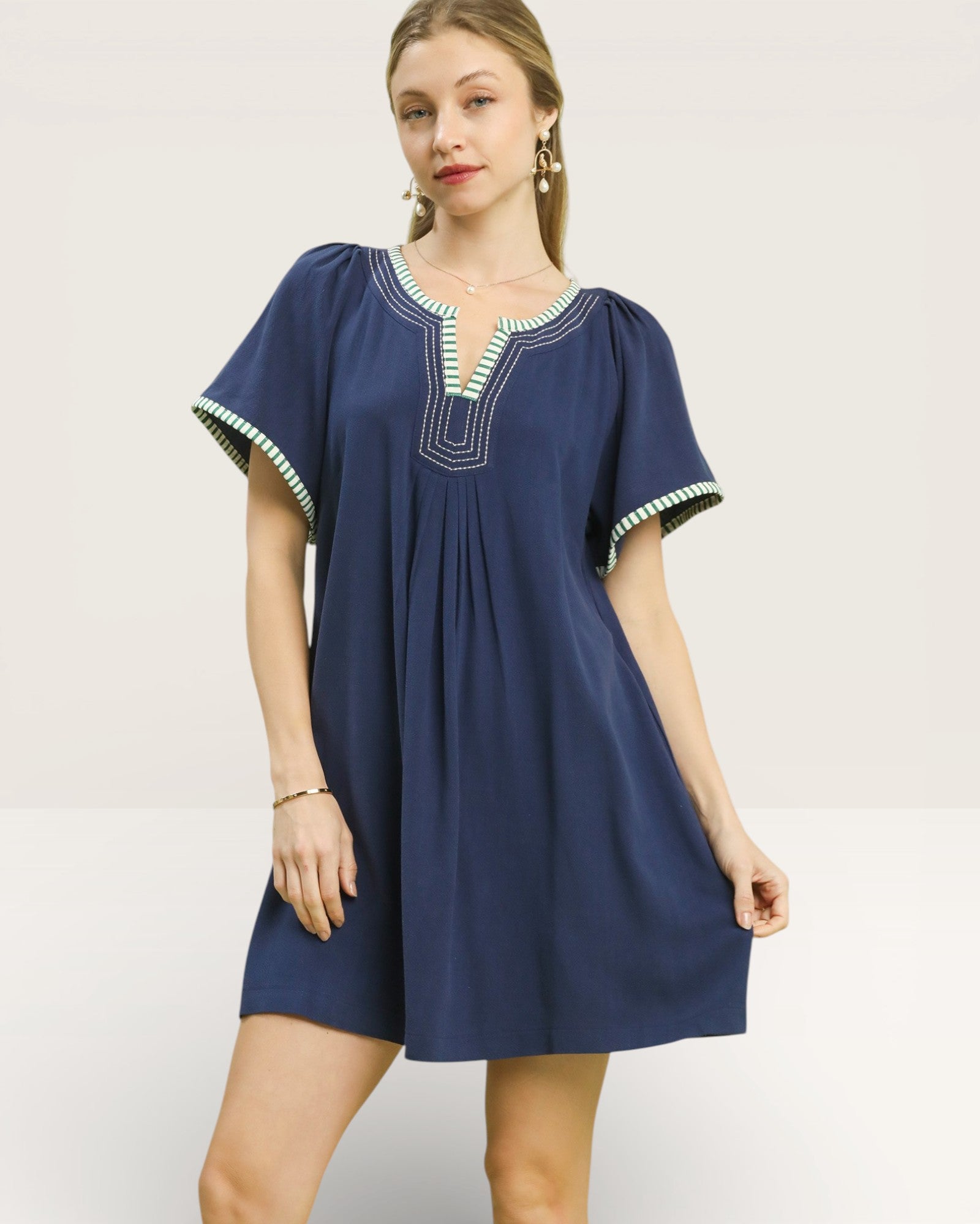 Woman wearing a navy blue dress with white trim on a plain background