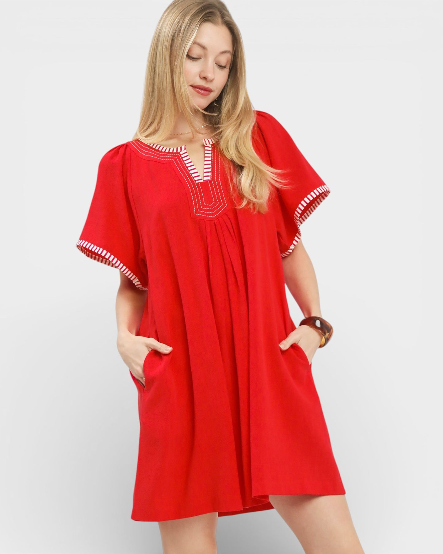 Woman wearing a red dress with white embroidery on a plain background