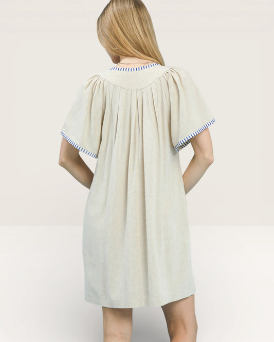 Woman wearing a beige dress with blue trim on a white background