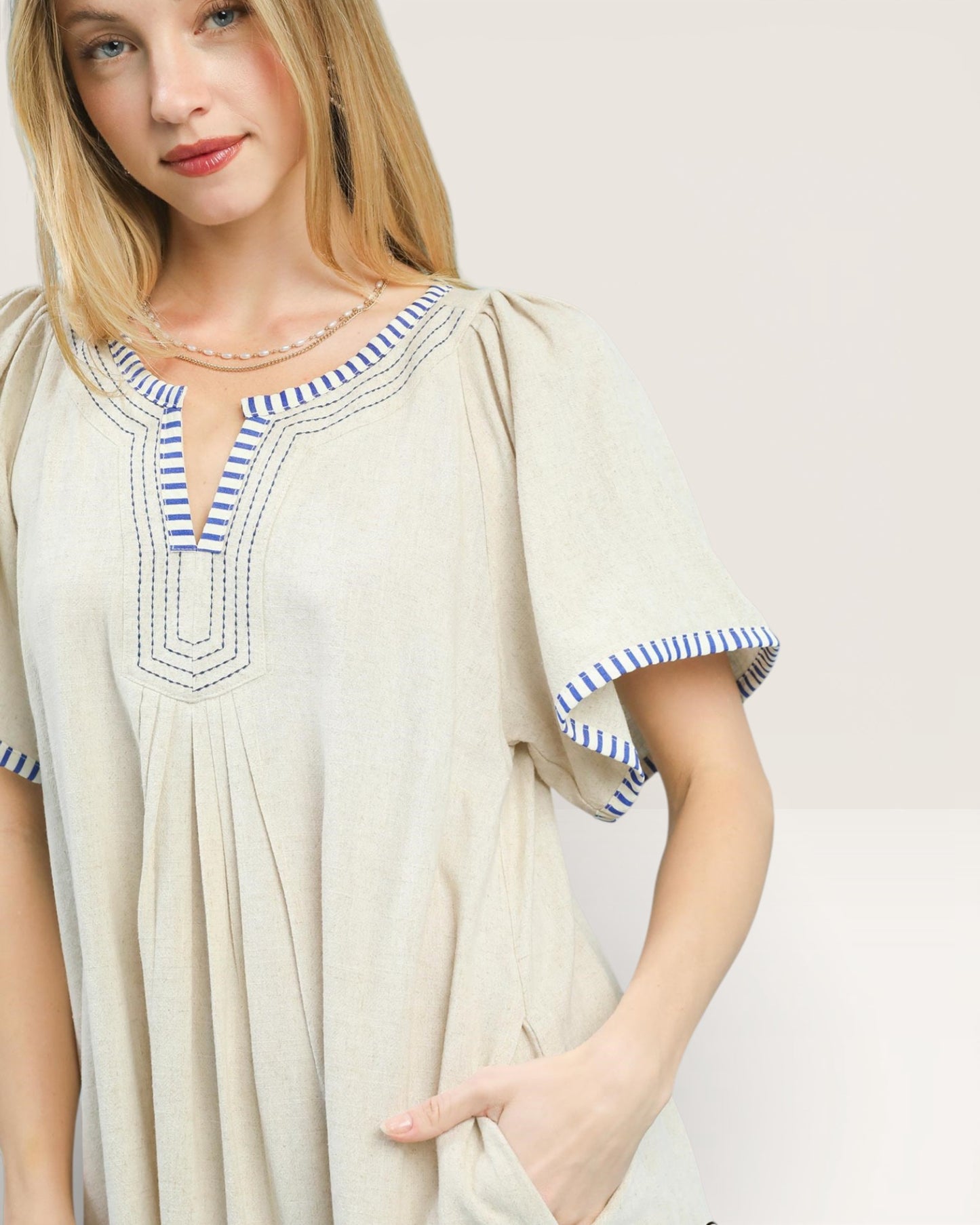 Woman wearing a beige dress with blue accents on a plain background