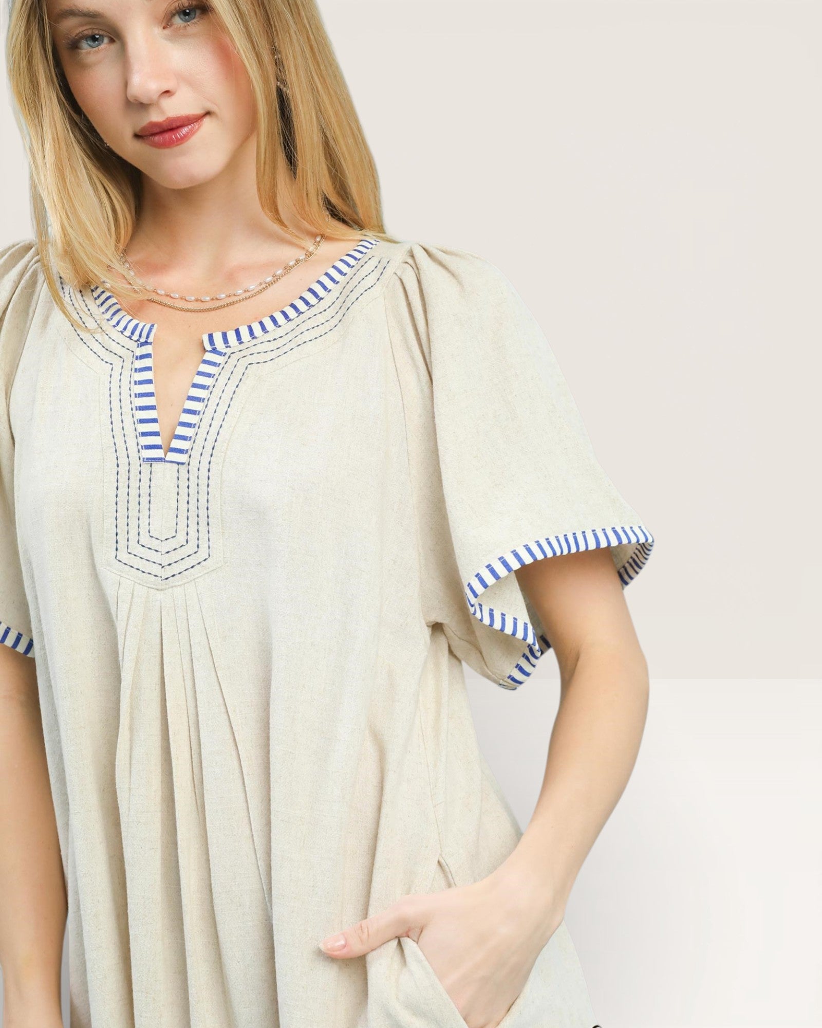 Woman wearing a beige dress with blue accents on a plain background