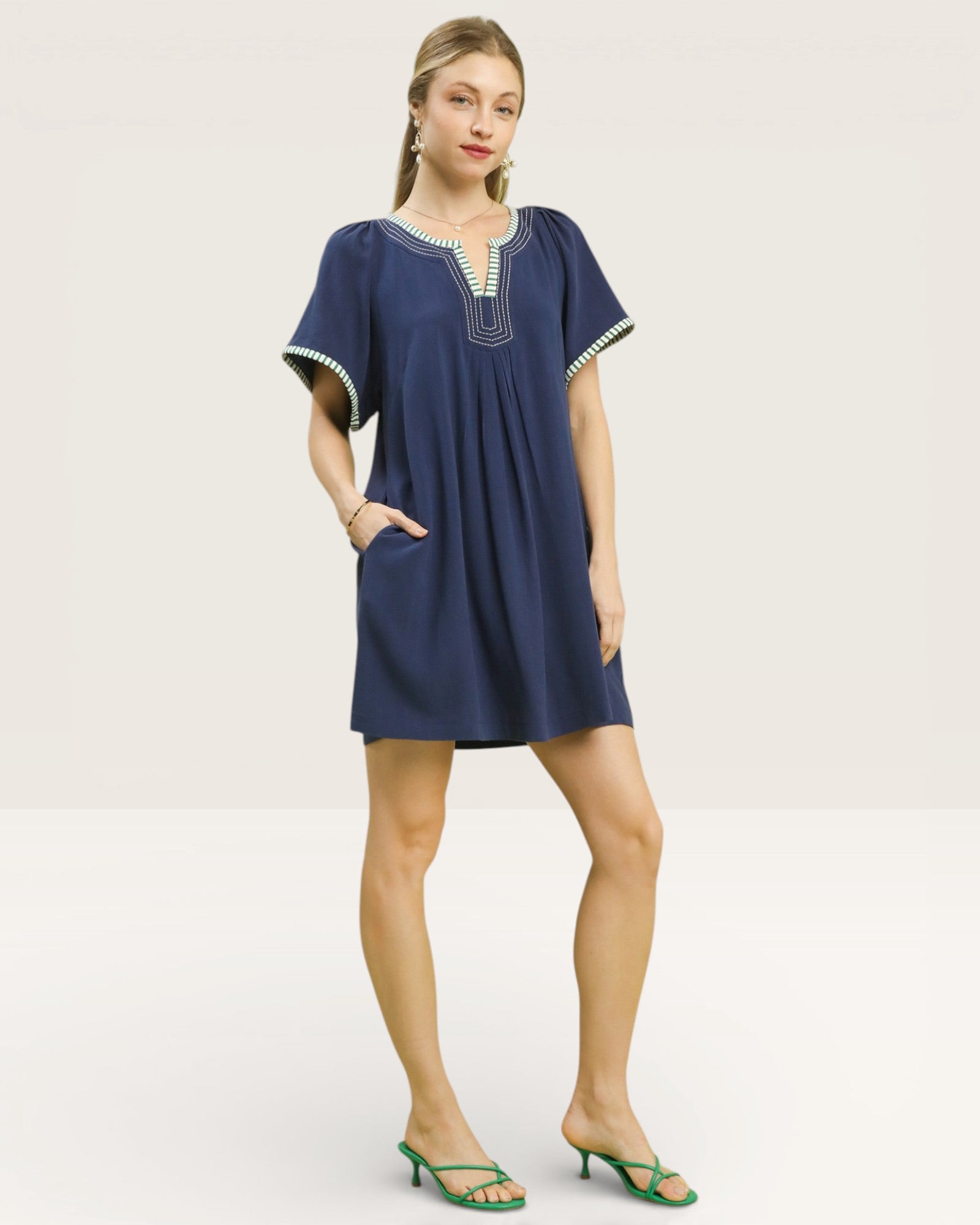 Woman wearing a navy blue dress with white embroidery on a light gray background