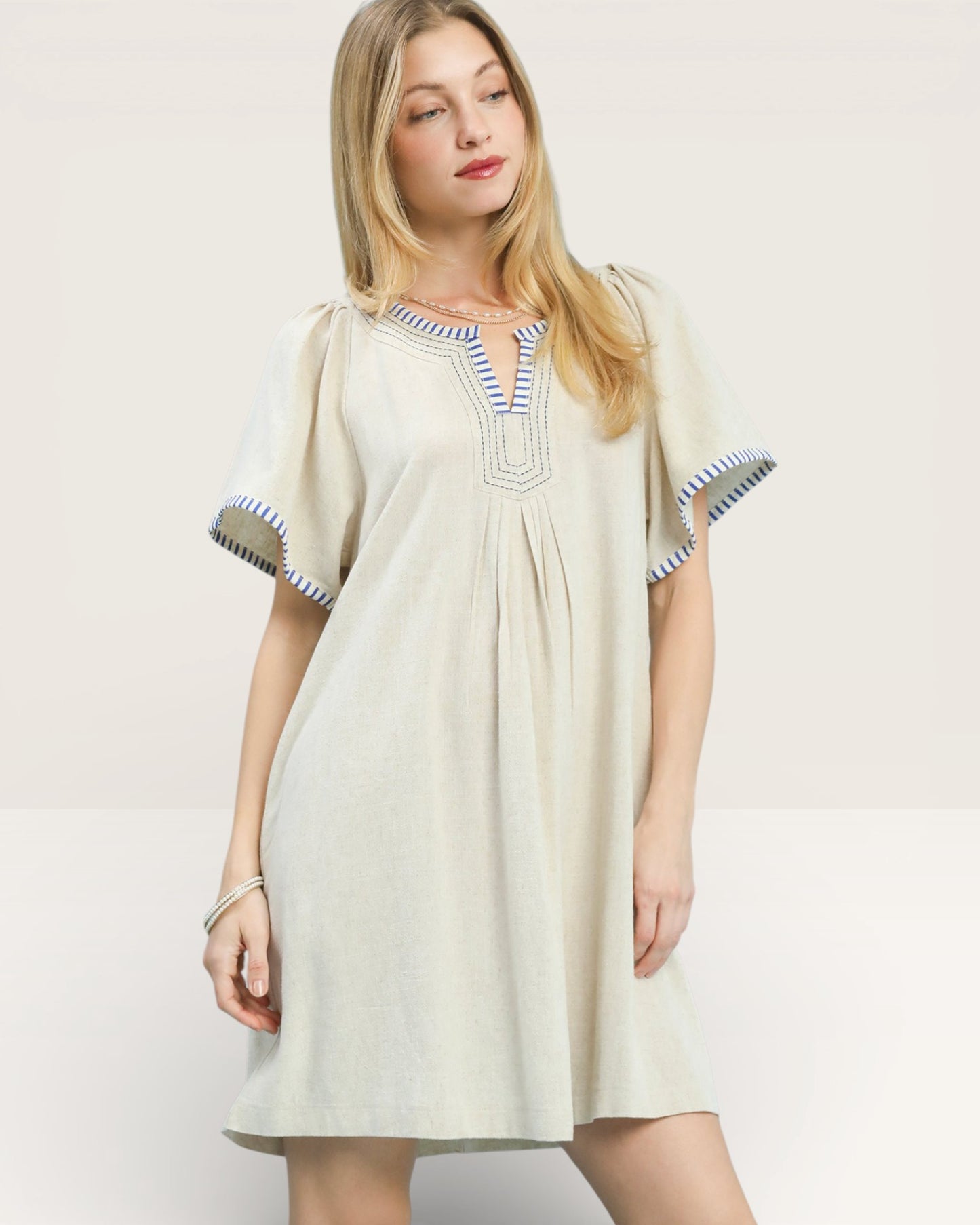 Woman wearing a beige dress with blue trim on a white background