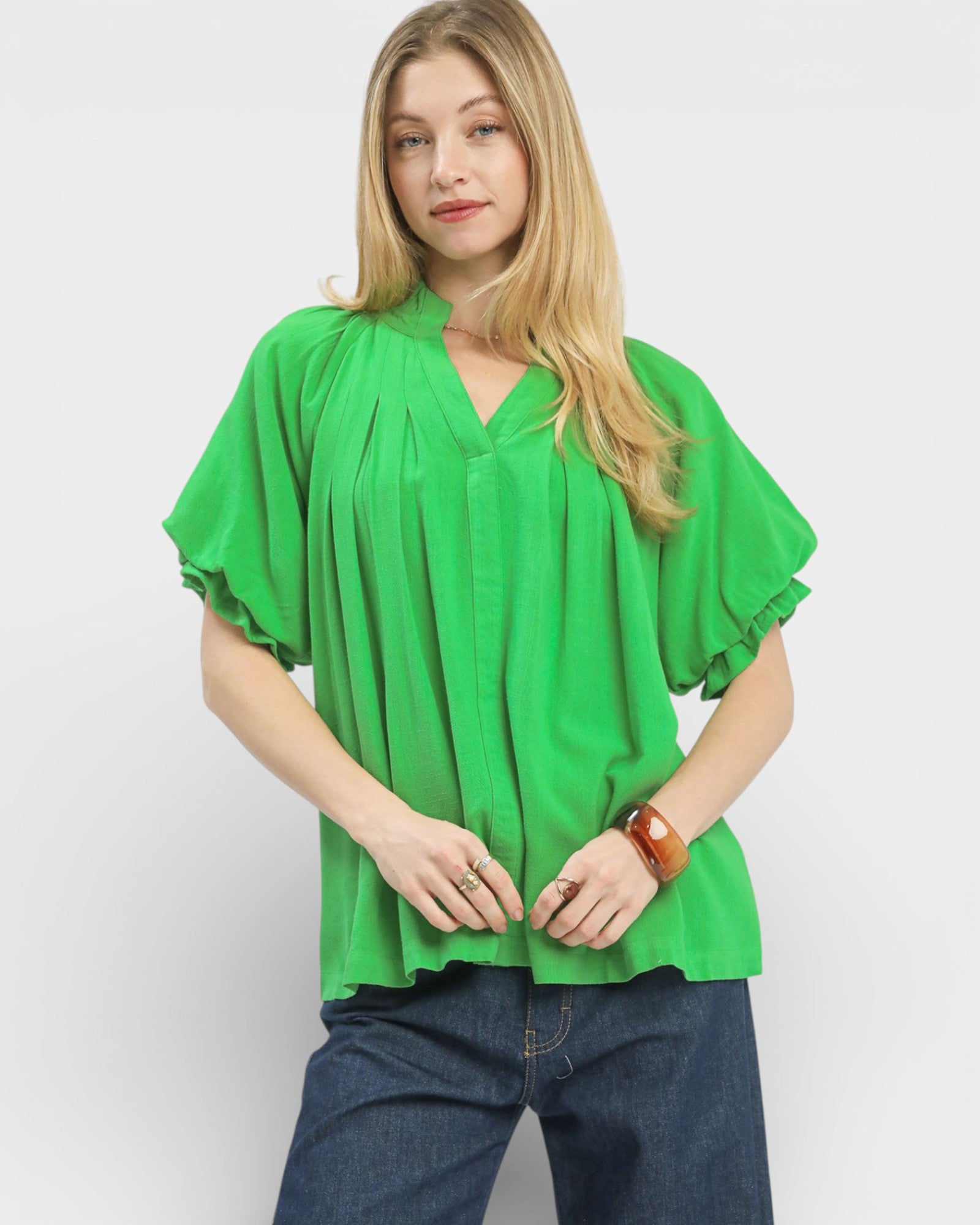 Woman wearing a green blouse with ruffled sleeves on a plain background