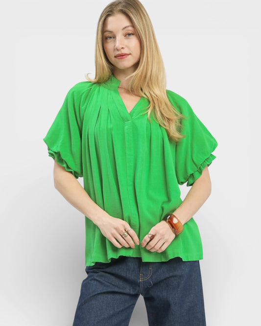 Woman wearing a green blouse with ruffled sleeves on a plain background