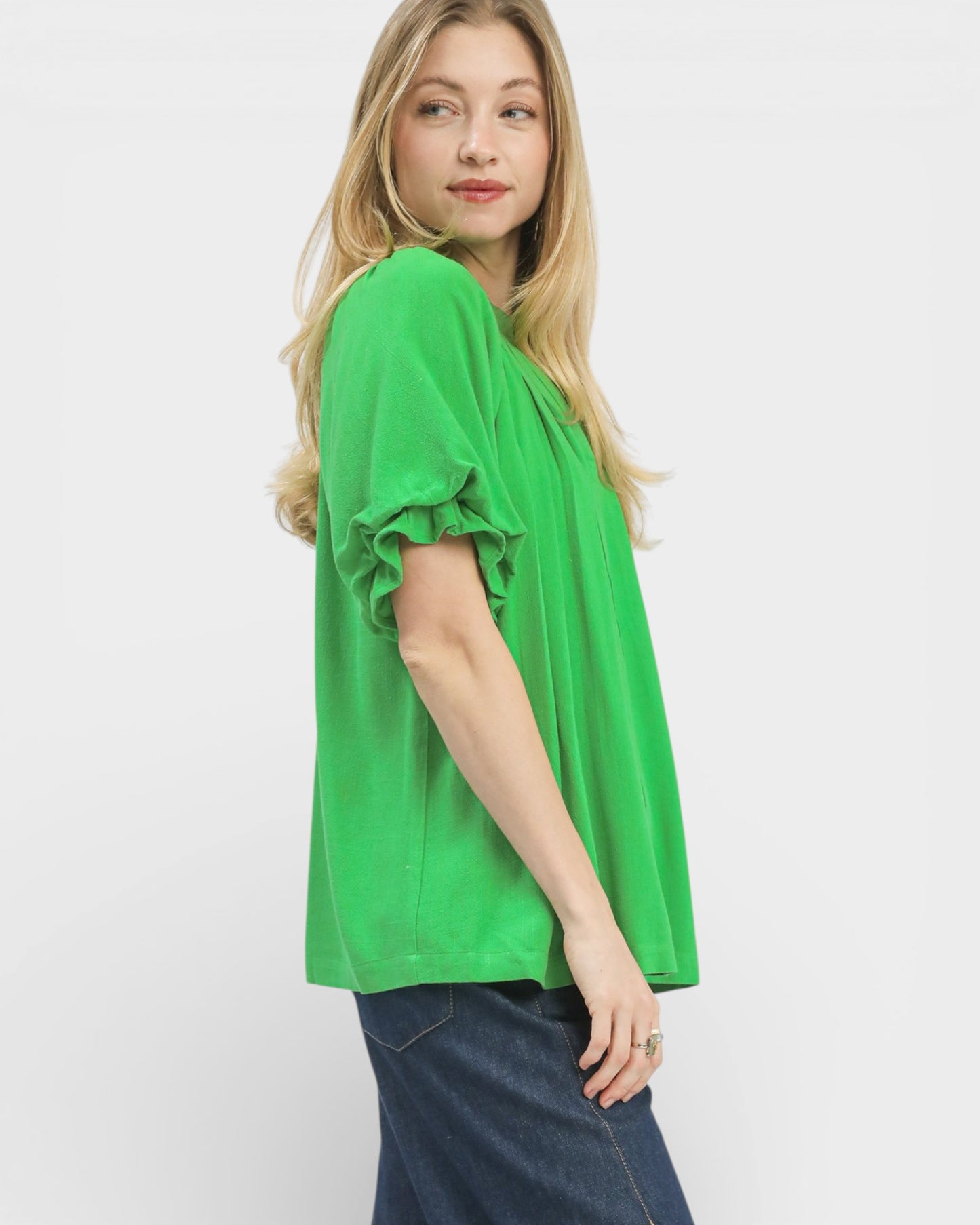 Woman wearing a bright green top with ruffled sleeves on a white background