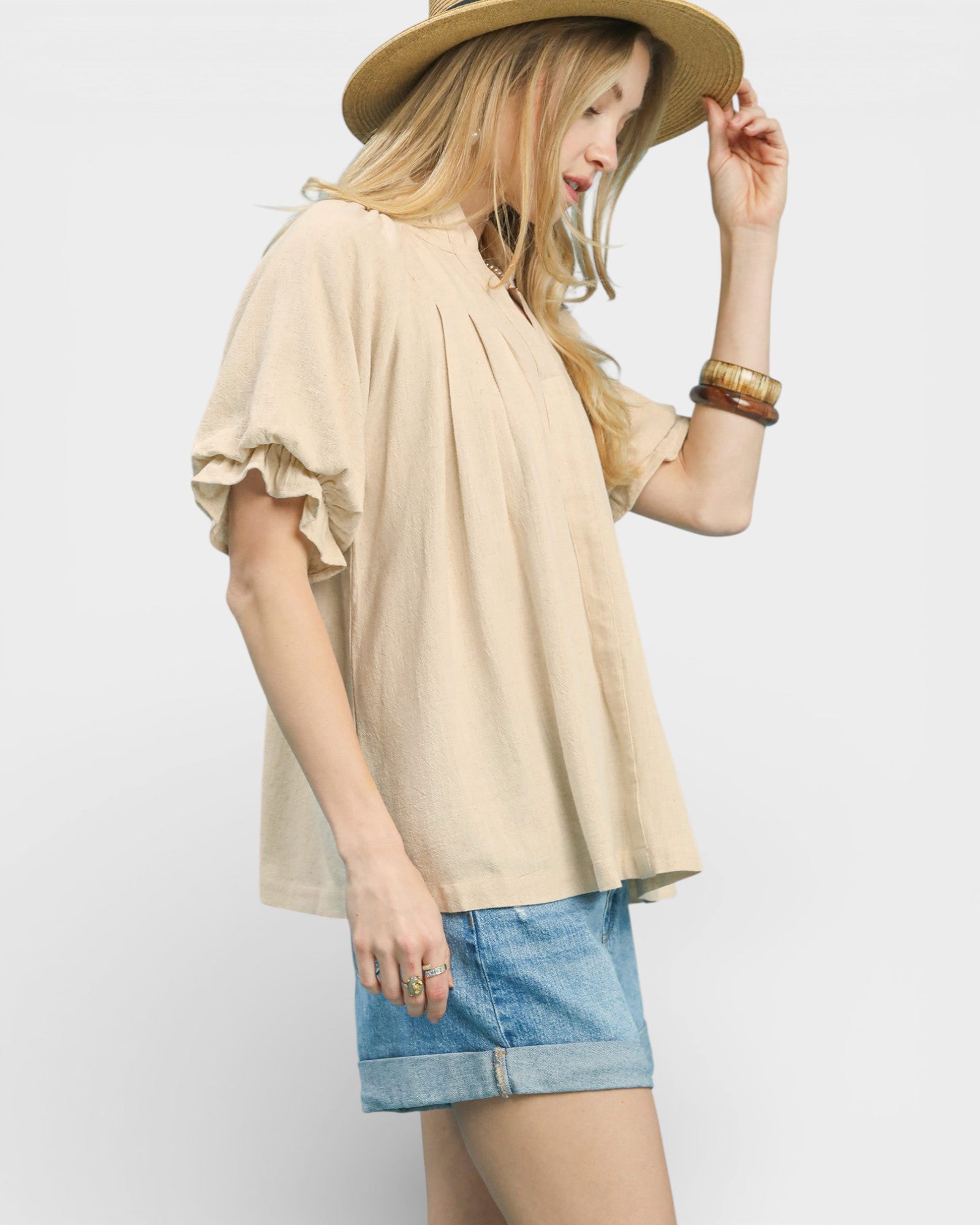 Woman wearing a beige blouse, blue shorts, and a hat on a plain background