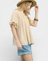 Woman wearing a beige blouse, blue shorts, and a hat on a plain background