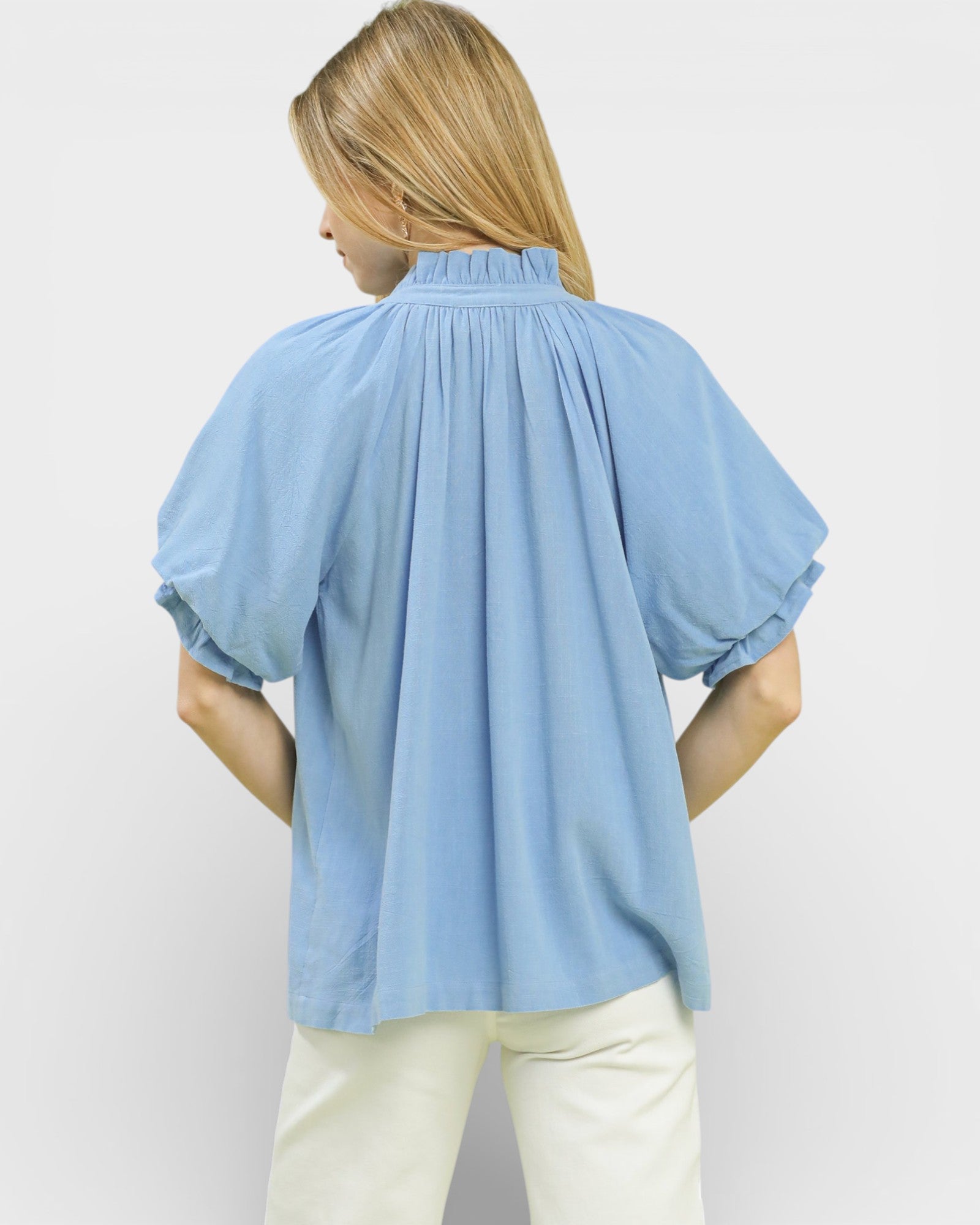 Woman wearing a light blue blouse with puff sleeves on a plain background