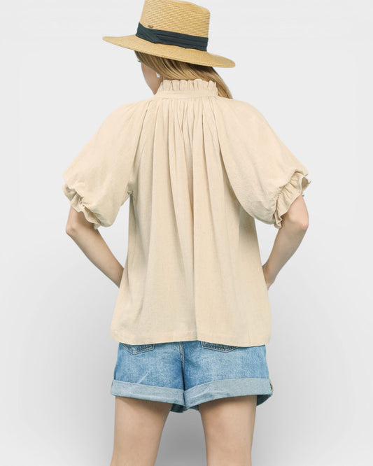 Person wearing a beige blouse and denim shorts with a straw hat on a white background