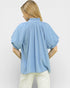 Woman wearing a light blue blouse with puff sleeves on a plain background