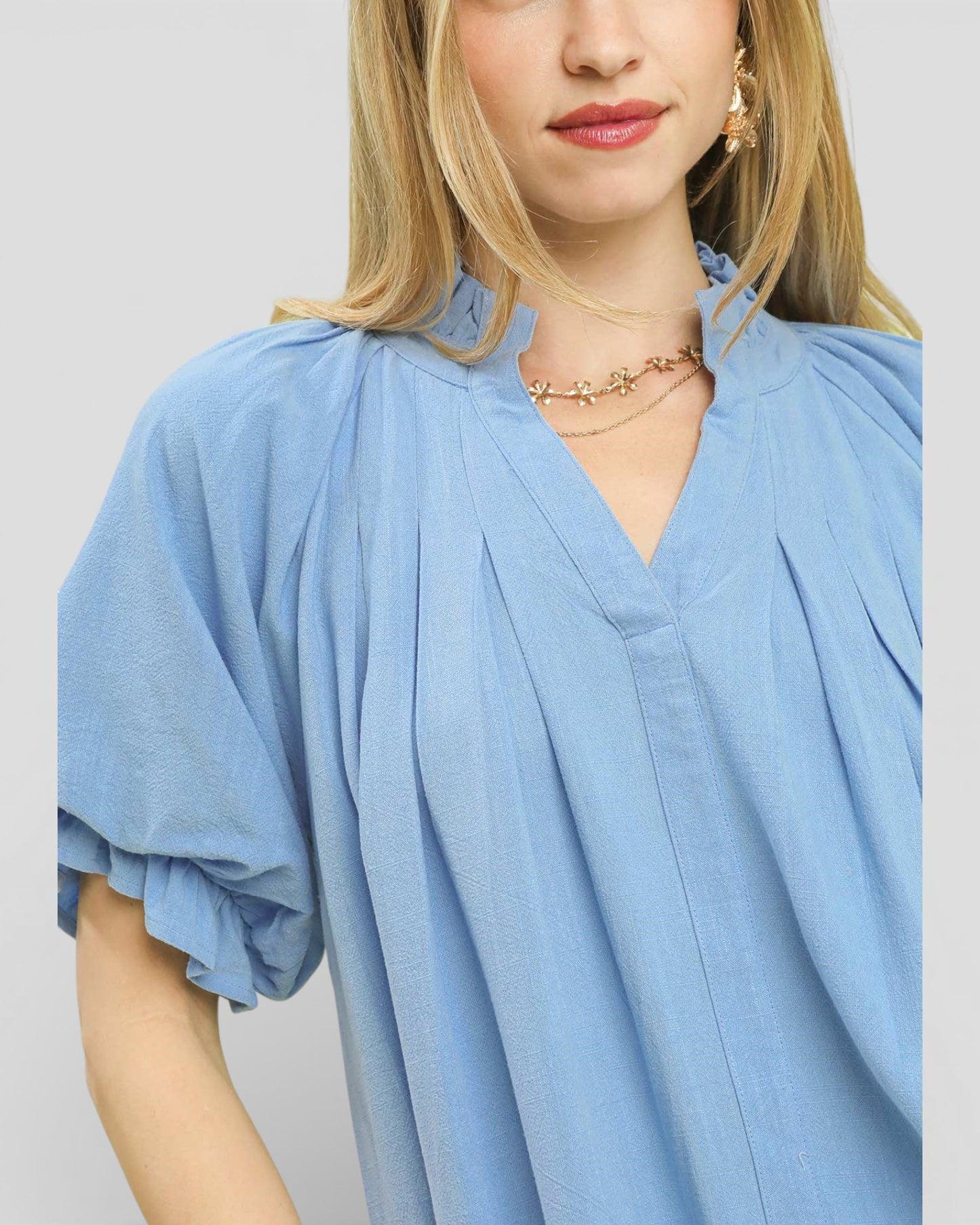 Woman wearing a light blue blouse with ruffled sleeves on a plain background