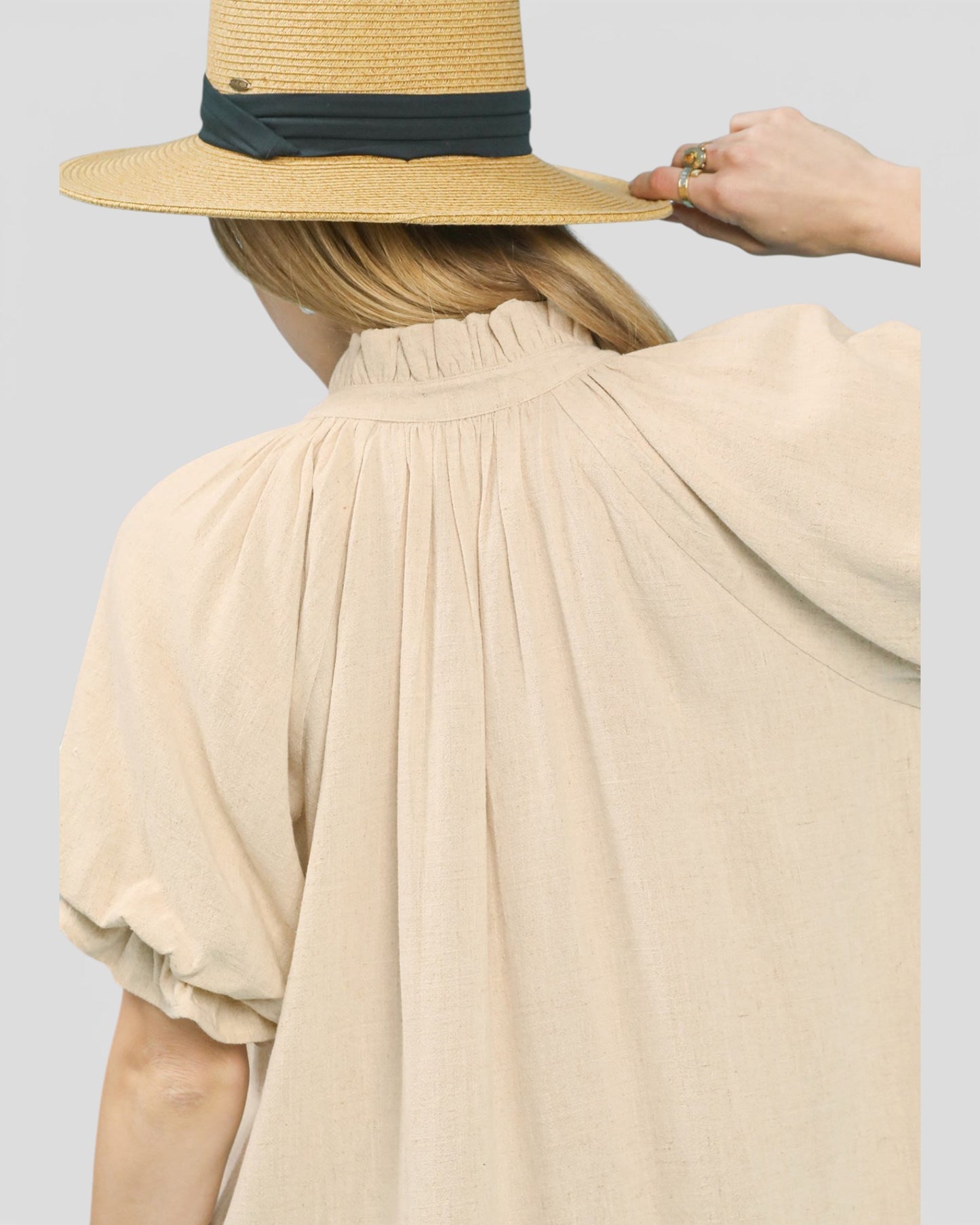 Person wearing a wide-brimmed straw hat with a black band on a plain background