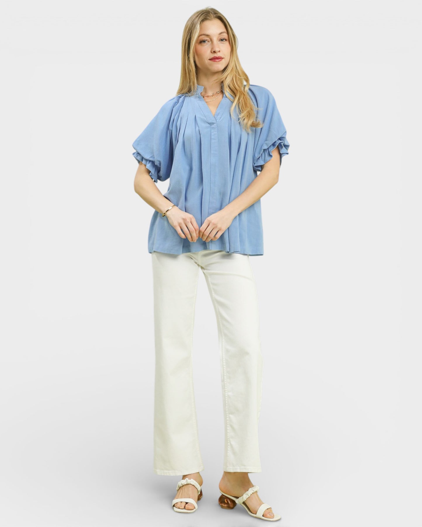Woman wearing a blue blouse and white pants on a plain background
