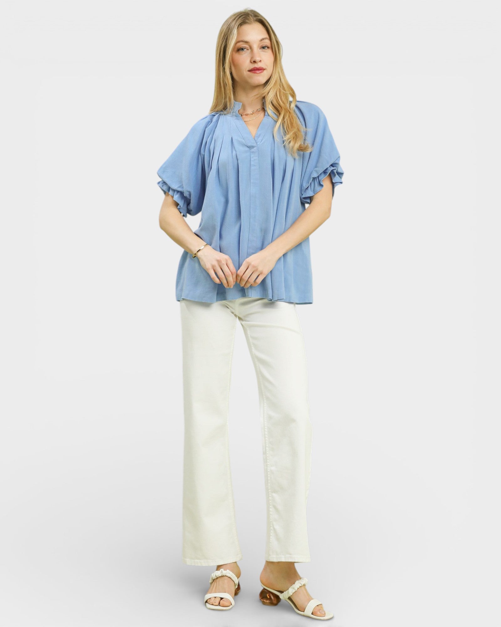 Woman wearing a blue blouse and white pants on a plain background