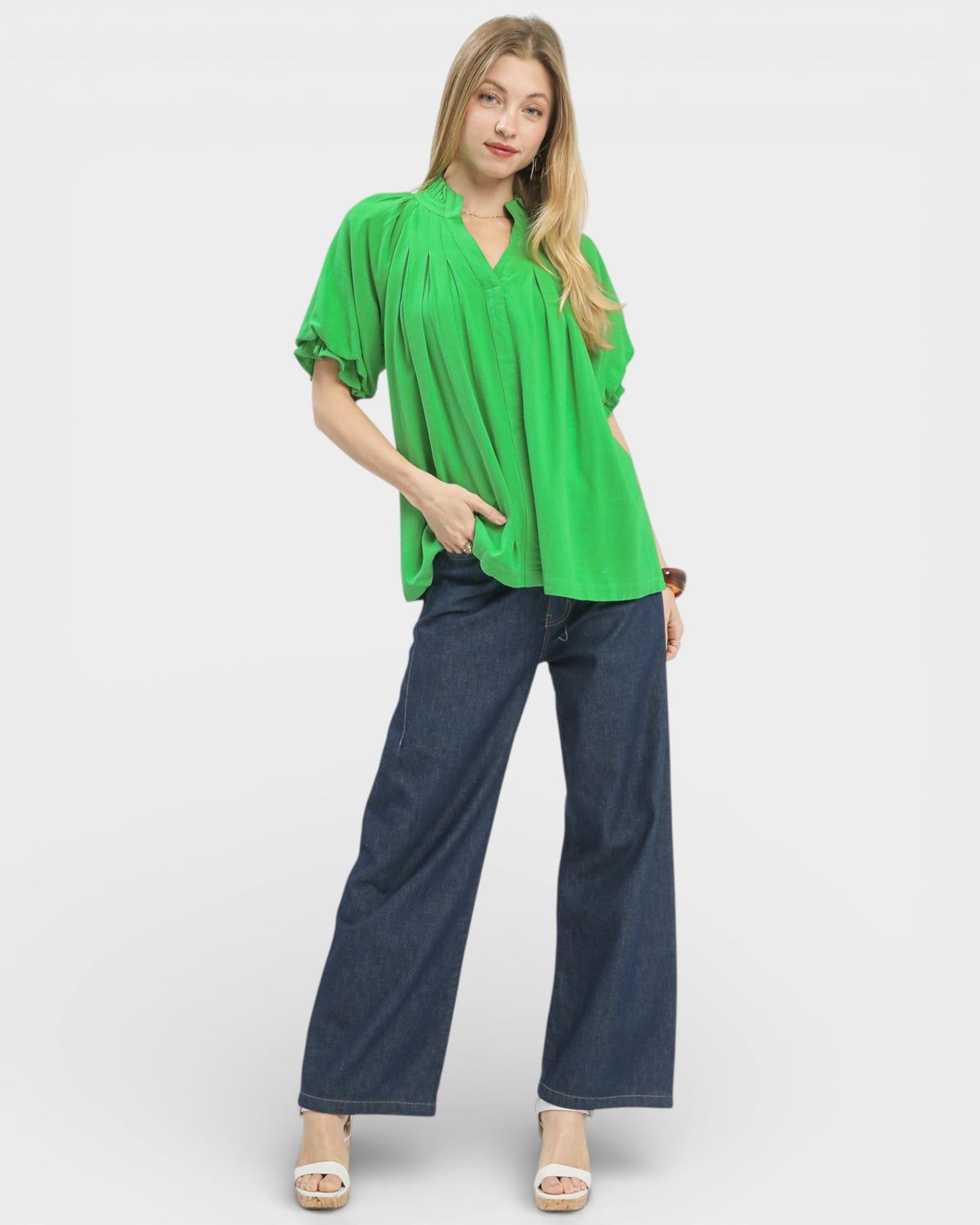Woman wearing a bright green blouse and blue jeans on a white background