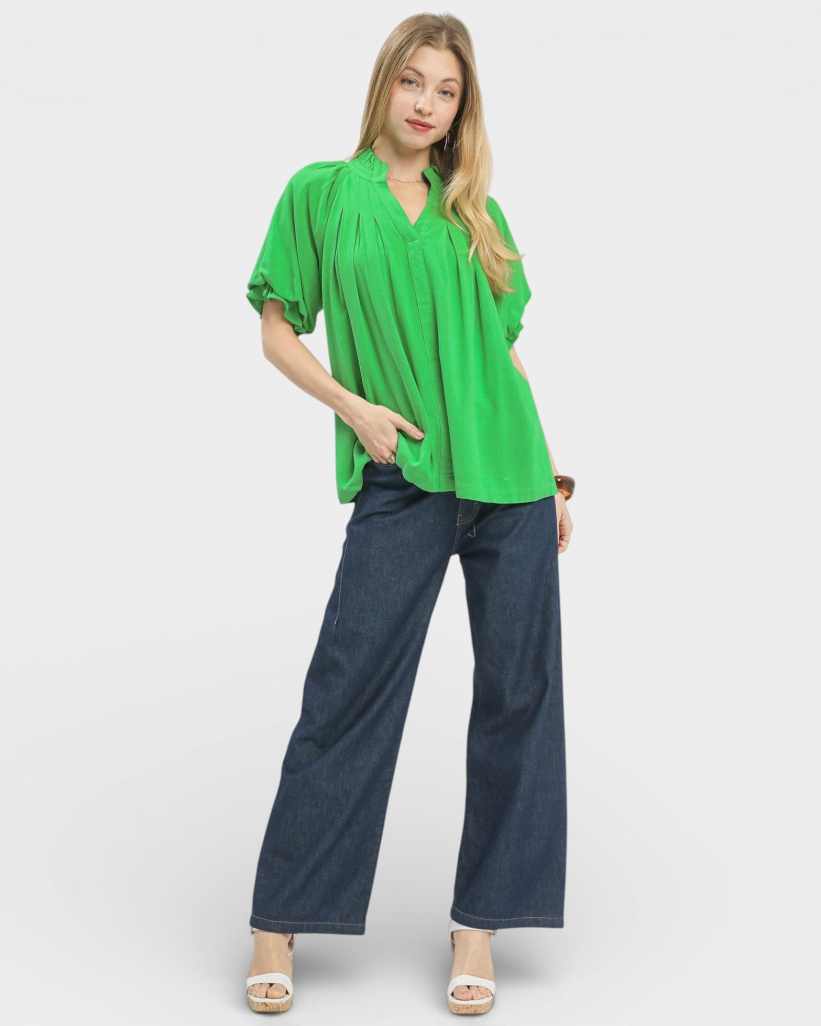 Woman wearing a bright green blouse and blue jeans on a white background