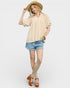 Woman wearing a beige blouse, denim shorts, and a straw hat on a white background