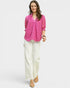 Woman wearing a pink blouse and white pants on a light gray background