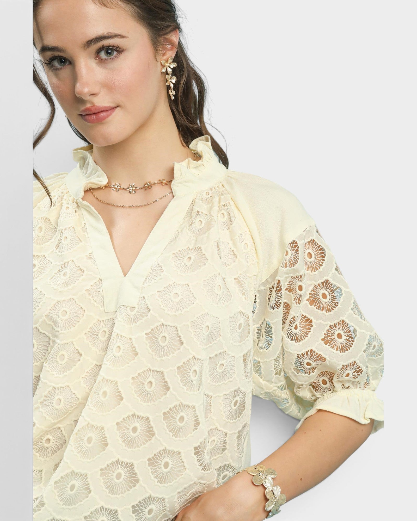 Woman wearing a light-colored lace blouse with floral patterns on a plain background