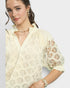 Woman wearing a light-colored lace blouse with floral patterns on a plain background
