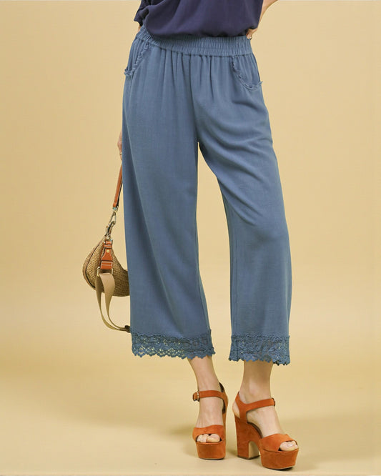 Blue wide-leg pants with lace trim worn by a person on a beige background