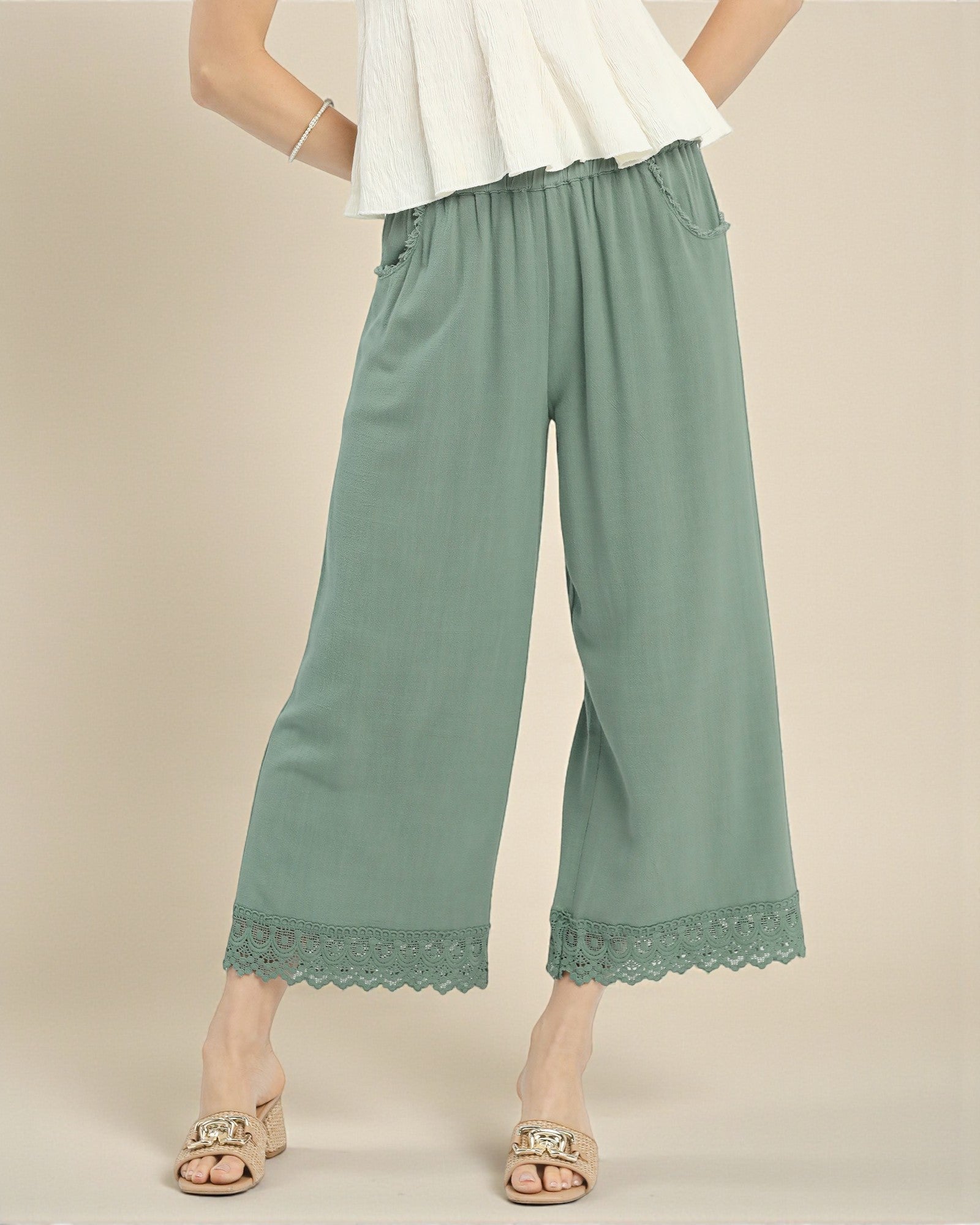 Green wide-leg pants with lace trim worn by a person on a beige background