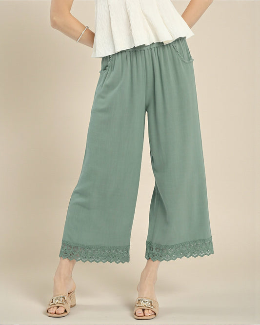 Green wide-leg pants with lace trim worn by a person on a beige background