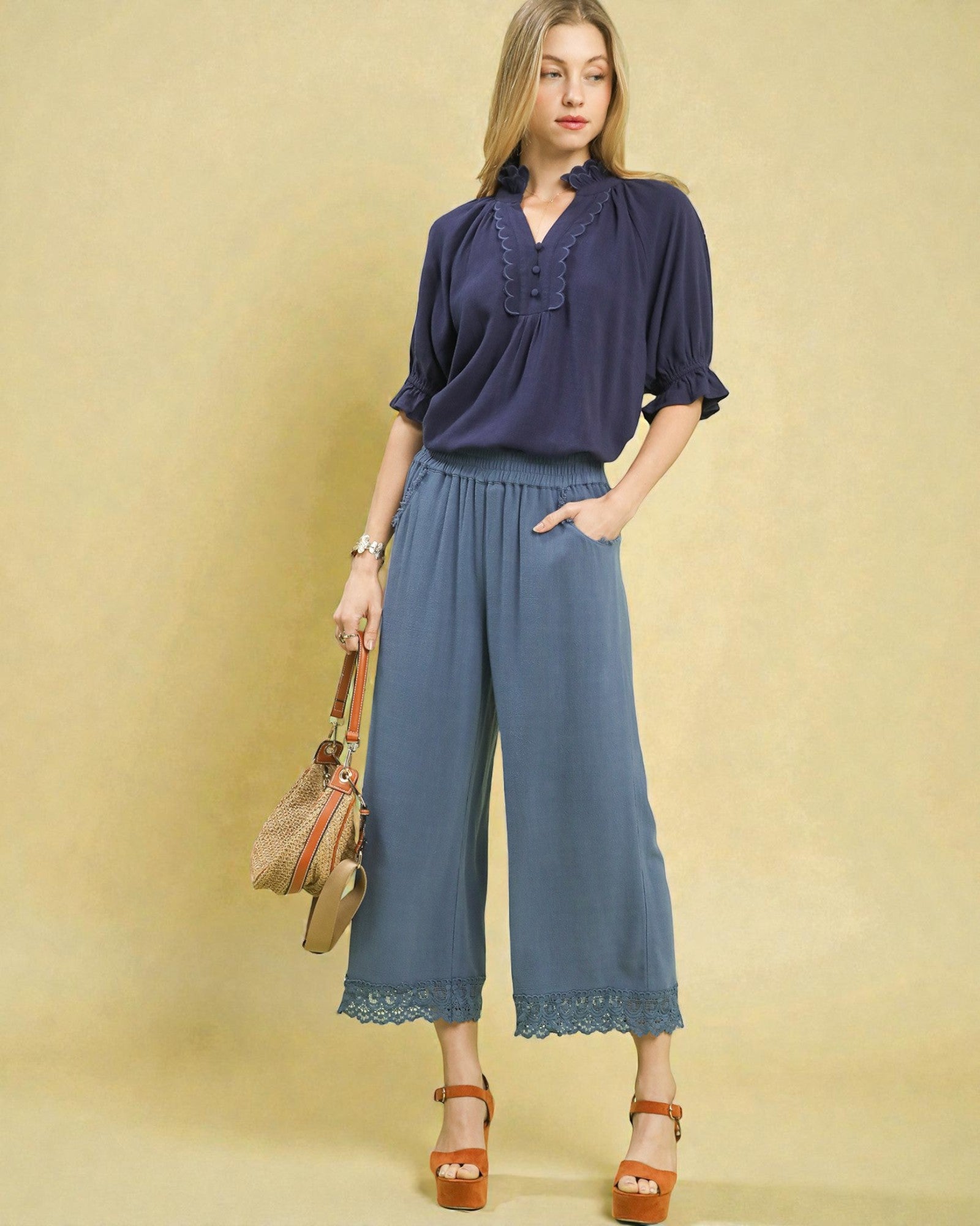 Woman wearing a navy blouse and blue wide-leg pants against a beige background