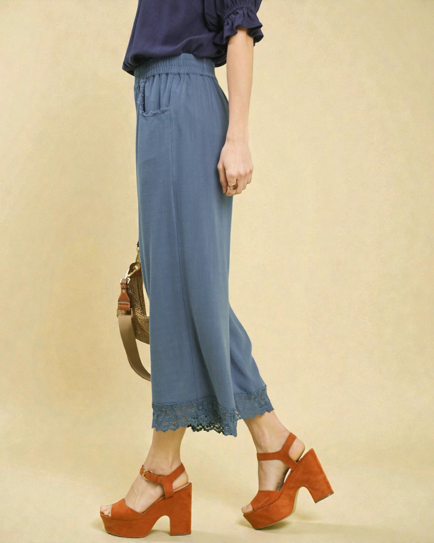 Person wearing blue pants with lace trim and orange sandals on a beige background