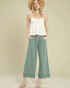 Woman wearing a white top and green wide-leg pants with a beige background