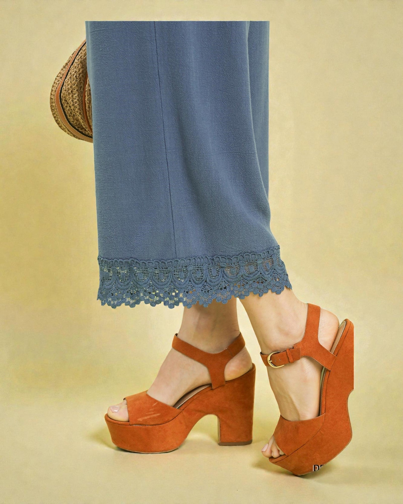Orange platform sandals worn with blue pants on a beige background