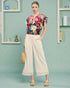 Woman wearing a colorful floral blouse and white pants against a light blue background