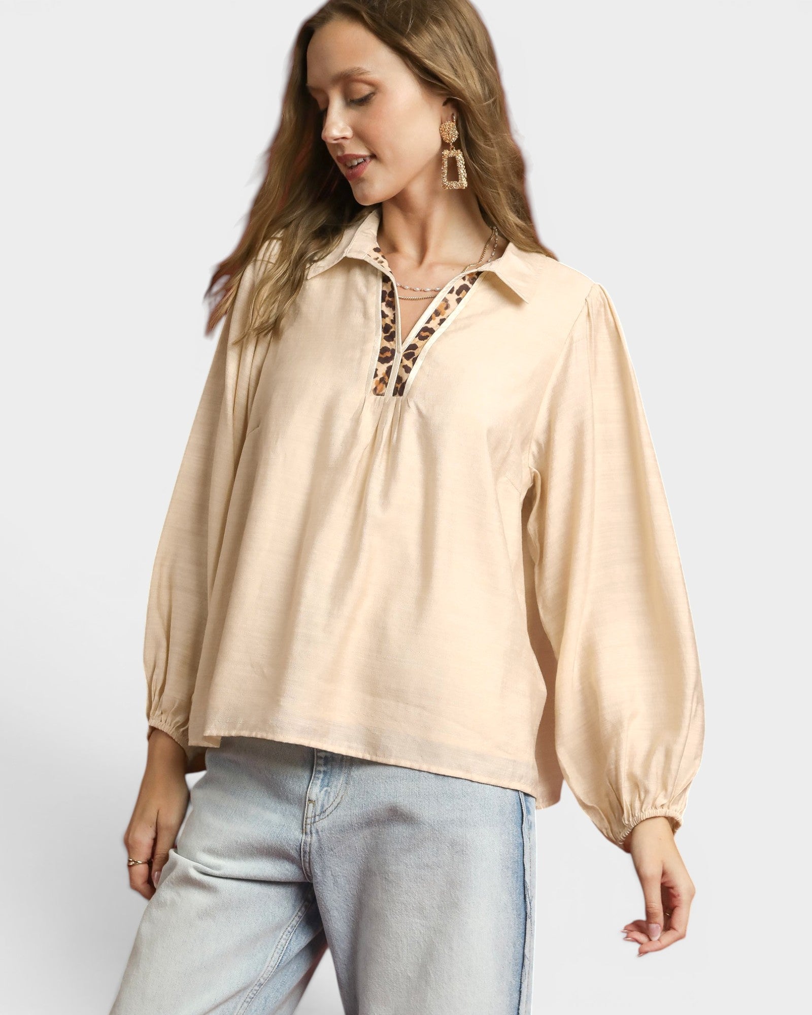 Woman wearing a beige blouse with long sleeves and light blue jeans on a white background