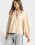 Woman wearing a beige blouse with long sleeves and light blue jeans on a white background