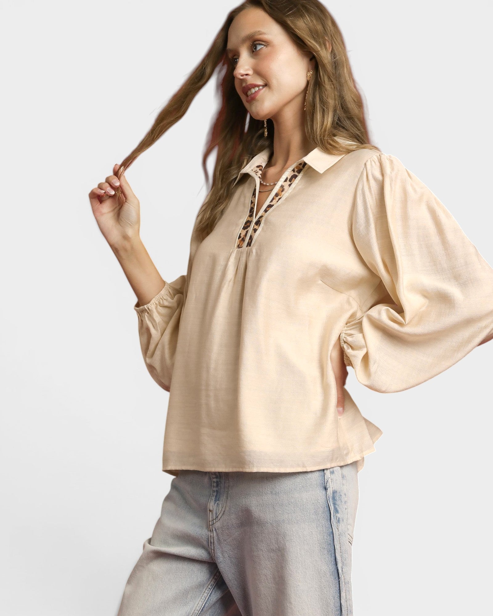 Woman wearing a beige blouse with leopard print details on a white background