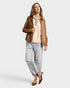 Woman wearing a brown leather jacket, beige top, and light blue jeans on a white background