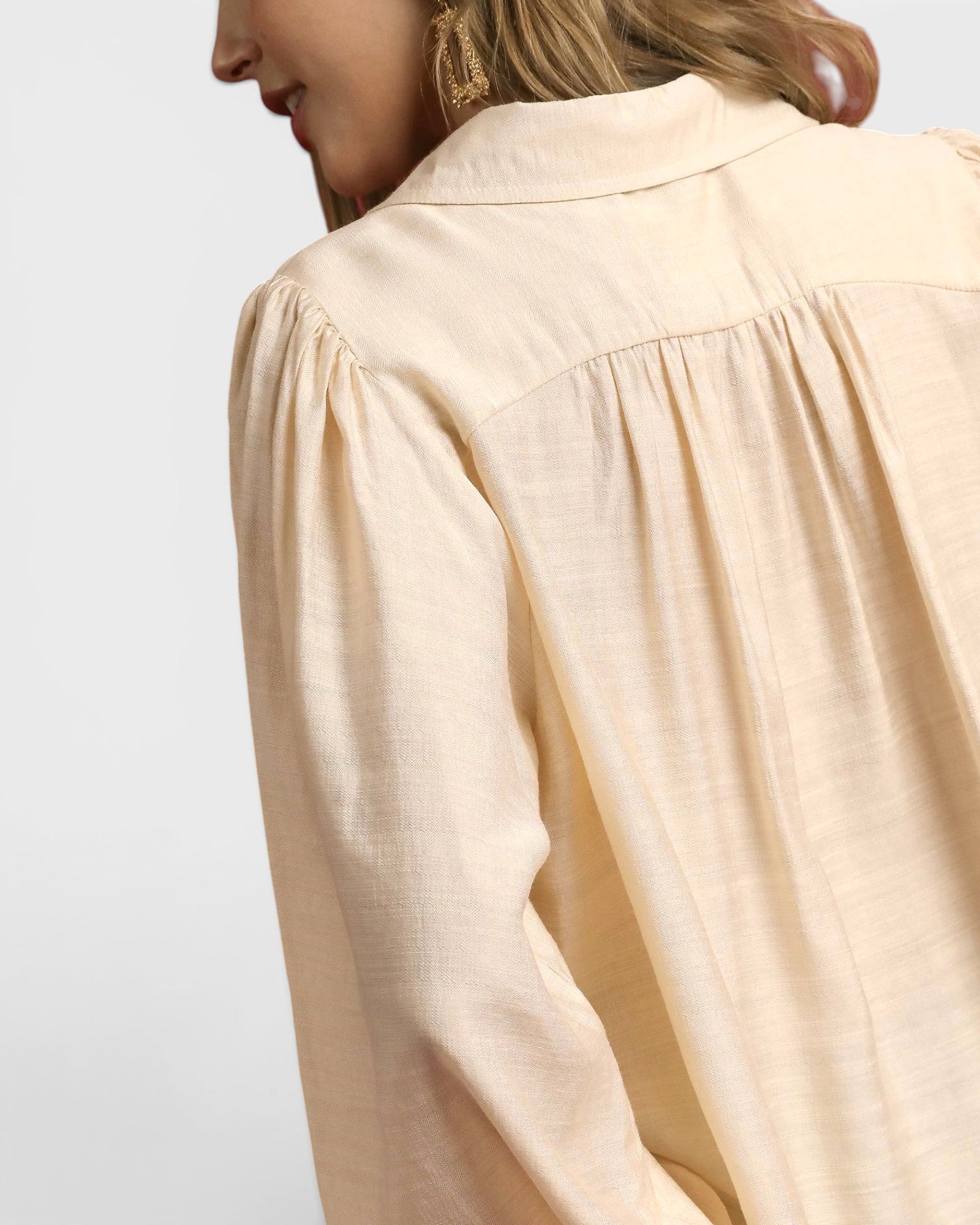 Beige blouse worn by a person on a light gray background