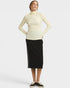 A woman modeling a cream ribbed mock neck long-sleeve top and a black midi skirt with white side stripes, paired with black and white sneakers, against a light gray studio background.