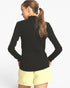 A woman shown from the back wearing a black long-sleeve mock neck top and light yellow shorts against a plain white background.