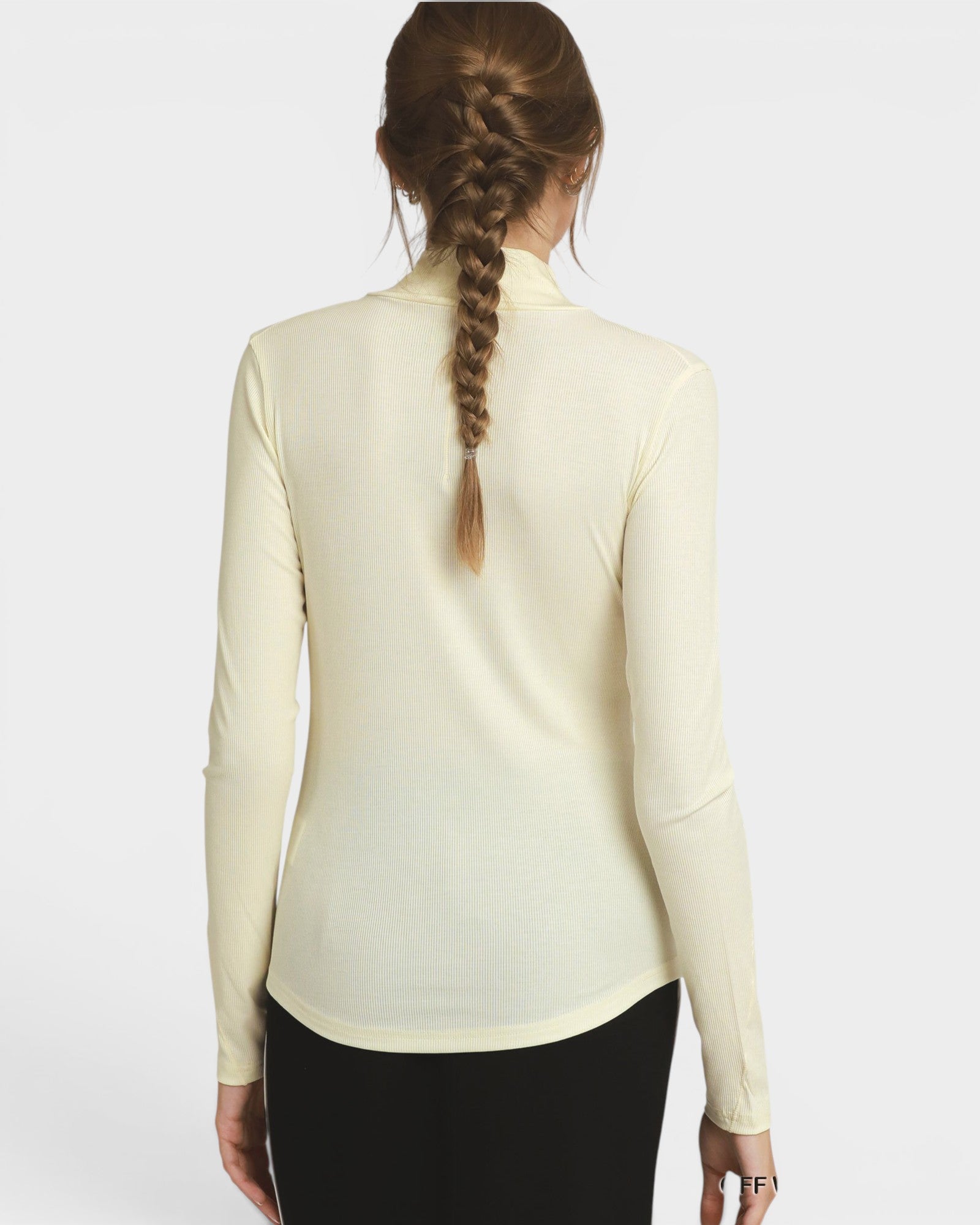 A woman viewed from the back wearing a fitted long-sleeve mock-neck top in a warm off-white/cream color, paired with black bottoms, against a light gray studio background.