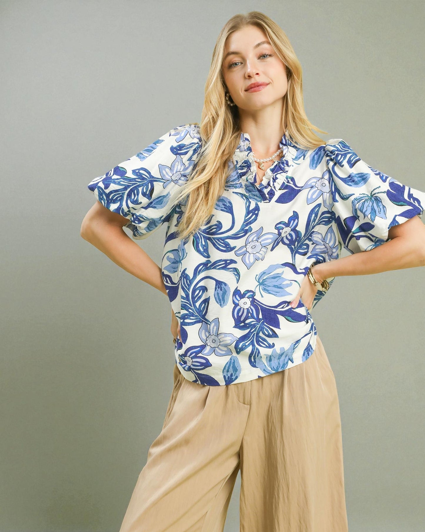 Woman wearing a blue floral blouse and beige pants against a gray background